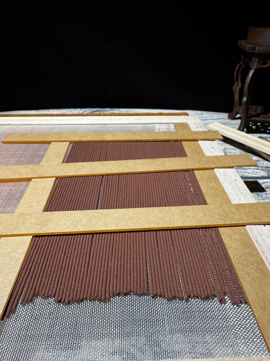Natural botanical incense sticks resting on a wooden mesh drying rack in an artisan studio