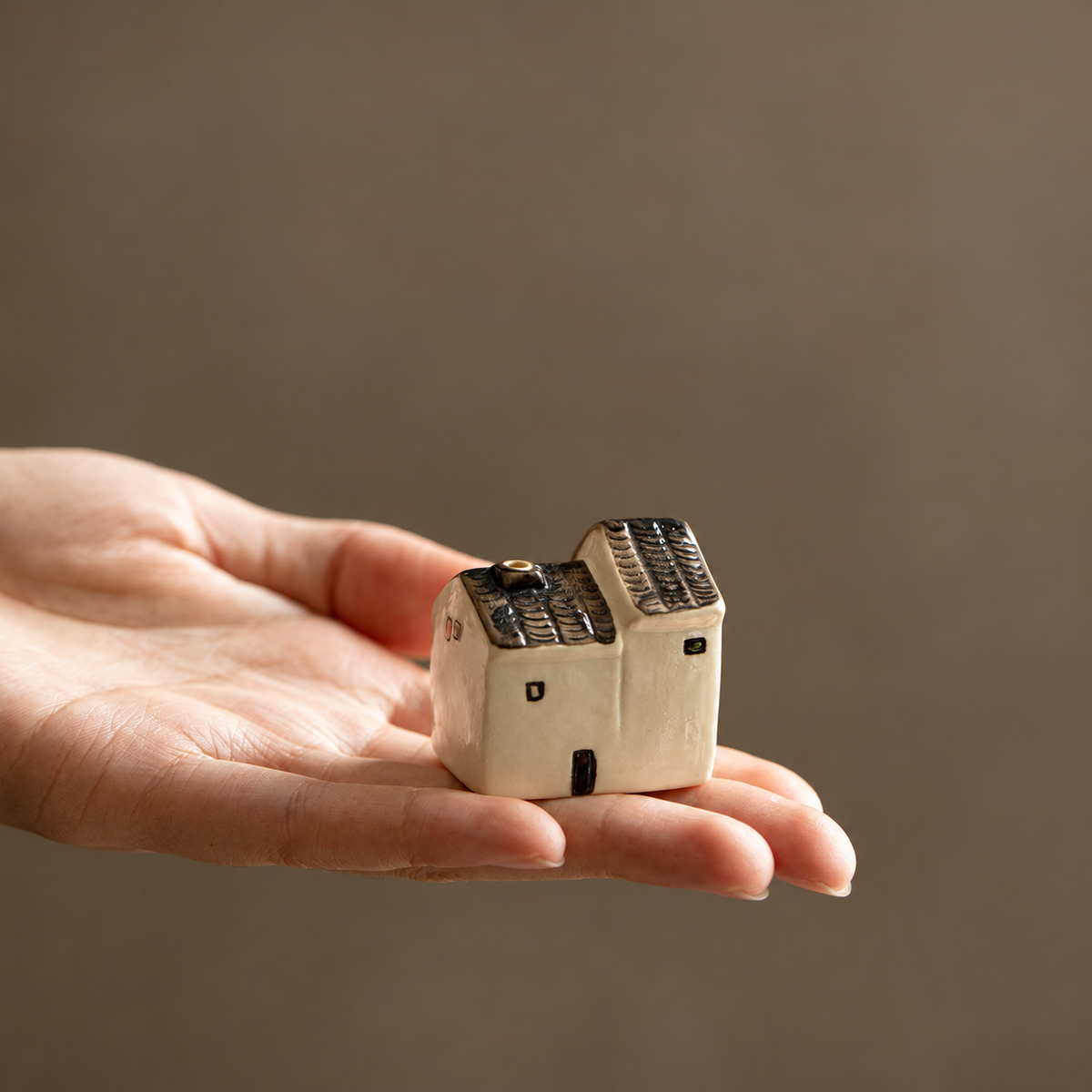 Short ceramic house incense holder resting on a hand to show its compact size
