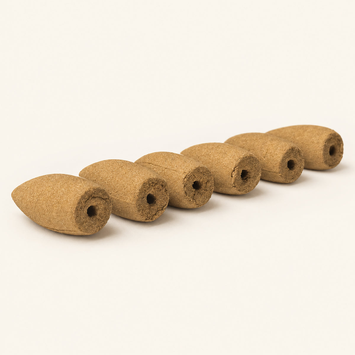 Close-up of six handmade backflow incense cones showing central base holes on an ivory background